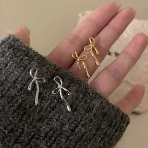 Detail view of gold and silver bow stud earrings held on a hand for scale and texture