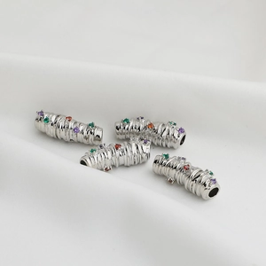 Macro detail of silver curved tube beads with colorful zircon inlay on white fabric