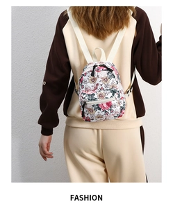 Girl wearing small floral backpack over a hoodie against a clean white wall