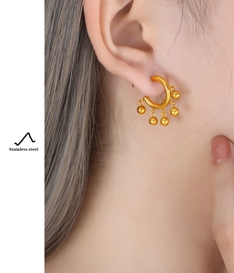 Close-up of gold C-shaped stainless steel earrings with five dangling beads on ear