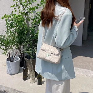 Detail of off-white quilted crossbody bag featuring gold chain strap and green buckle