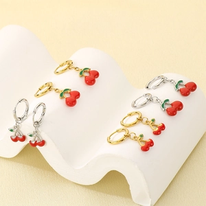 Detail of red cherry pendant earrings in gold and silver finishes on white texture