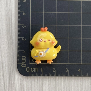 Close-up of a small yellow resin chicken charm with egg bag on a centimeter scale mat