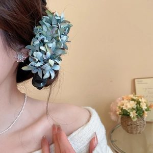 Detail of a large blue fabric flower hair clip worn by a model in a cozy home setting