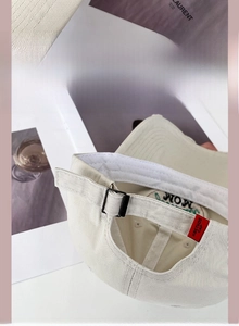 Detail of beige cotton baseball cap featuring adjustable metal buckle and red side label