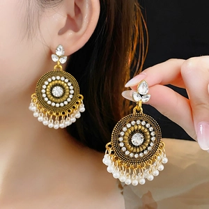 Dettaglio di orecchini vintage dorati con strass scintillanti e nappe di perle bianche
