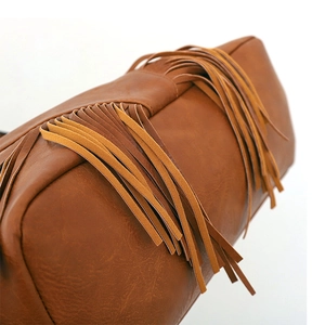 Gros plan détaillé sur la texture du cuir caramel et les franges en daim du sac hobo