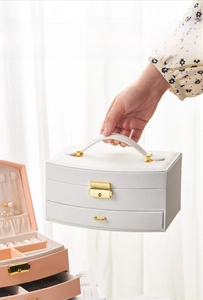 Close-up of white leather multi-layer jewelry box with gold metal lock and handle