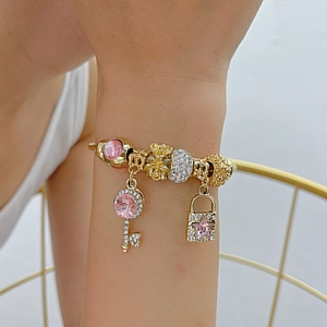 Golden beaded charm bracelet with pink crystal key and padlock pendants on model's wrist