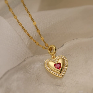Close-up of gold heart pendant with red gemstone and diamonds on white fabric