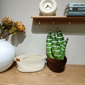 Vue détaillée du cactus en peluche dans son pot doux à côté d'un panier tressé en coton