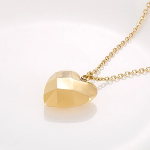 Gros plan du pendentif coeur doré 18K aux facettes géométriques sur une chaîne fine