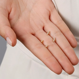 Close-up of gold rectangular bar earrings with zircon stones on a palm of hand