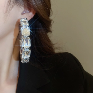 Macro detail of square-cut crystals on oversized silver hoop earrings worn by a model