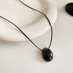 Gros plan du pendentif ovale noir poli sur un collier minimaliste en cordon de cire
