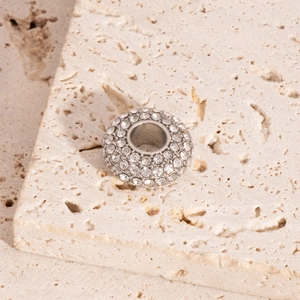 Macro view of a silver cylinder charm with clear rhinestones on a beige stone surface