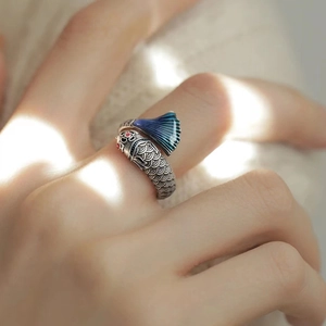 Macro detail of a silver koi fish ring with red and blue enamel accents on a finger