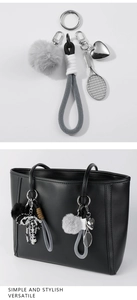 Detail view of heart and racket charms with a grey fur pompom on a black tote bag