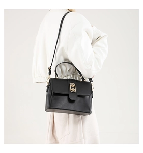 Detail of minimalist black crossbody bag featuring a golden oval metal lock and smooth matte leather