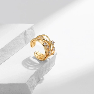 Minimalist golden wrap ring with wavy lines and small zircons on a white stone background