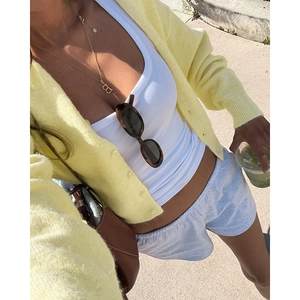Detailed flat lay of women's pale yellow knit cardigan with white ribbed tank top and shorts