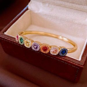Macro view of a gold-plated bangle with seven colorful gemstones on a beige jewelry box