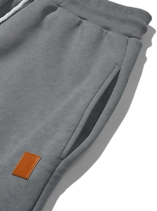 Detail view of grey sweatpants showing cotton texture, ribbed waist, and leather patch