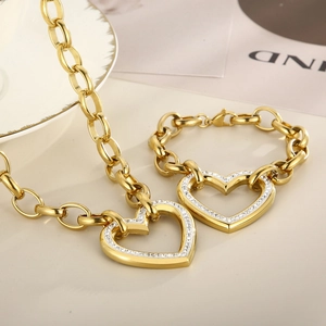 Close-up of chunky gold-plated chain set with rhinestone heart charms on a beige surface