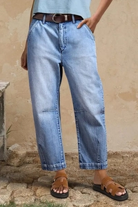 Détail d'un jean bleu clair avec fentes latérales sur l'ourlet et une ceinture en cuir brun