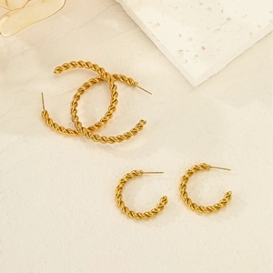 Golden twisted hoop earrings in multiple sizes on elegant stone texture background