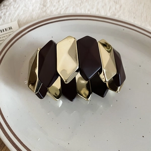 Detail of rhombic metal and resin bracelet in gold and dark brown on a white plate