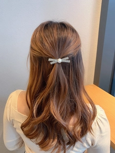 Detail of metal bow hair clip with sparkling rhinestones and a pearl on brown curly hair