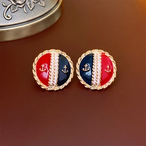 Detail of vintage round enamel earrings with golden anchor patterns on blue and red background