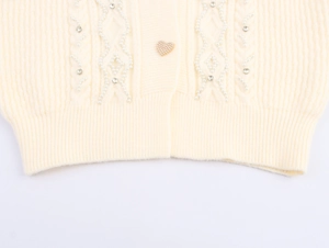 Detail of cable knit cardigan with pearl bead embellishments and a heart button