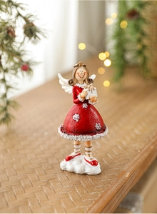 Detail of red and white resin Christmas angel figurine holding a gift box on a wooden desk