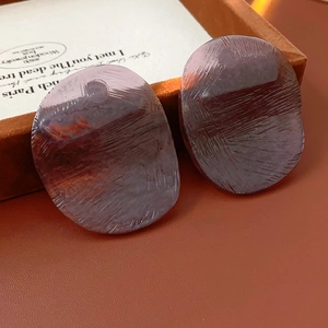 Detail view of purple irregular oval resin earrings on a wooden jewelry box background
