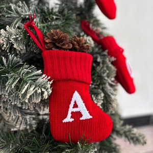 Red knitted Christmas stocking with white letter A embroidery hanging on a tree
