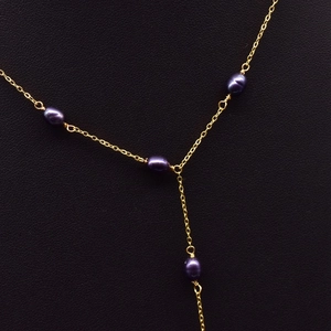 Y-shaped necklace featuring gold chain and dark pearls over a black fabric background