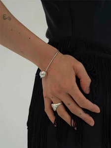Detail showing polished silver metal bracelet and chunky ring on a model with grey background