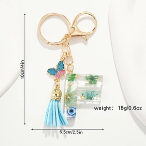 Close-up of resin letter F keychain with dried flowers, blue butterfly and tassel pendant