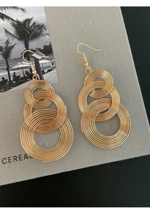 Macro shot of layered golden circular earrings on a textured linen surface with a beach photo