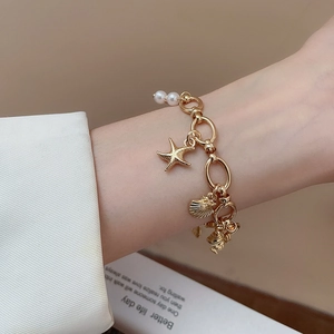 Golden ocean-themed pearl bracelet with starfish and shell charms worn on wrist