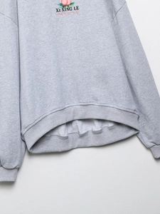 Détail d'un sweat gris clair avec poignets côtelés et broderie imprimée XI XING LE