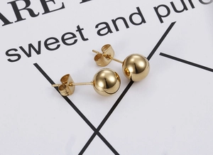 Close-up of polished gold spherical stud earrings with classic butterfly backings