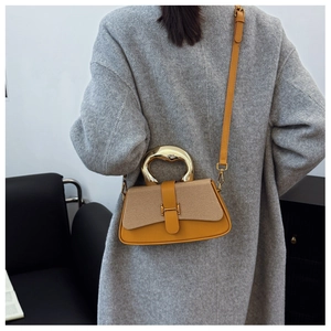 Detail view of yellow box bag with woven flap and gold metal ring handle on grey coat