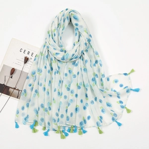 Close-up of white linen scarf featuring blue floral prints and two-tone fringe tassels