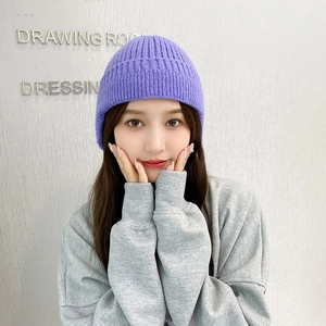 Detail of purple knitted beanie with ear flaps on female model for winter warmth