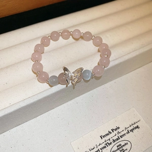Gros plan détaillé d'un bracelet en perles roses avec pendentif papillon argenté sur support