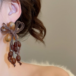 Close-up of vintage resin bow earrings with beaded tassels worn by a model
