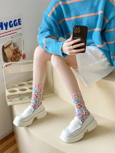 Detailed view of floral knit socks paired with white platform loafers on beige steps